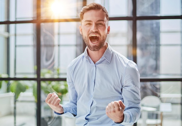 Photo portrait of a young businessman in a blue shirt shaking his fists celebrating his success