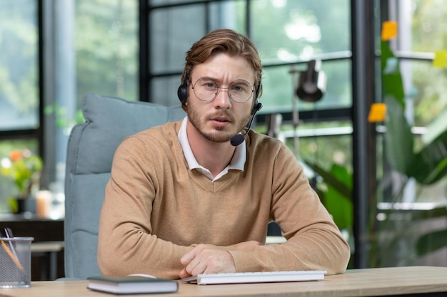 Portrait of a young businessman man in a headset working concentratedly from a home office speaks