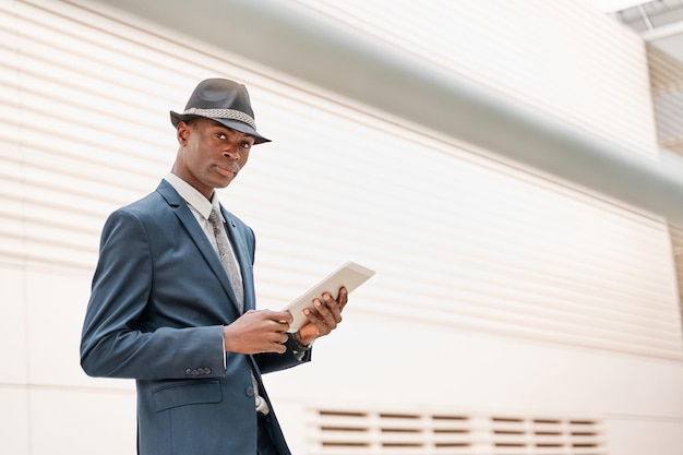 Portrait of a young businessman in a suit and hat using a tablet pc