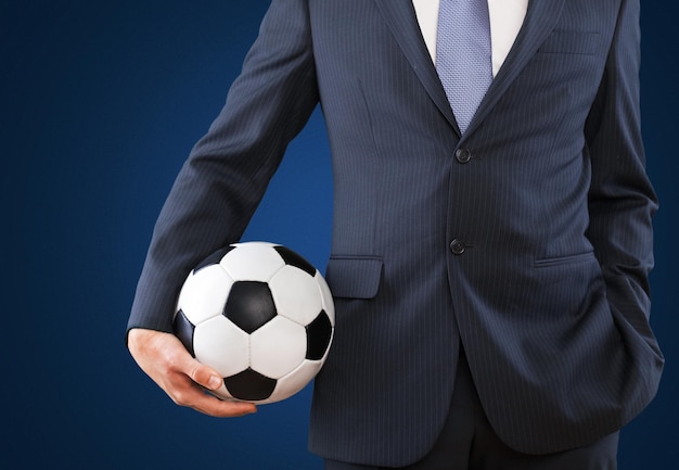 Portrait of young businessman in suit with football ball on background