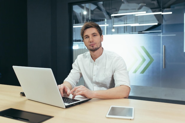 Portrait of young businessman with beard man working in modern office with laptop smiling and looking at camera