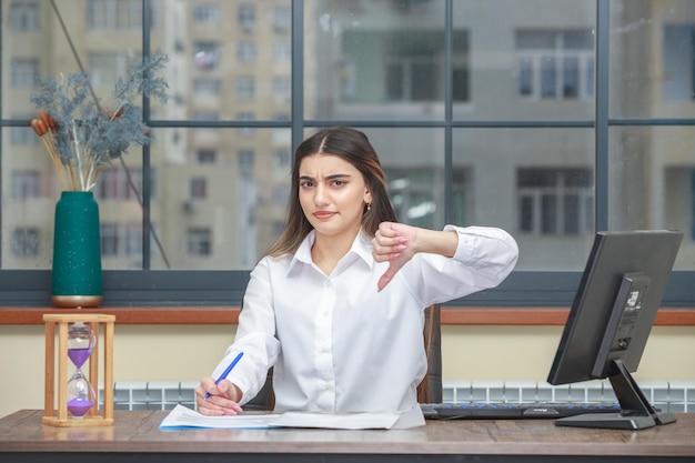 Portrait of a young businesswoman sitting at the desk and gesture thumb down