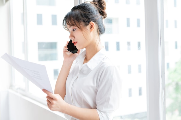 Portrait of young businesswoman standing by the window and making phone calls with her partner