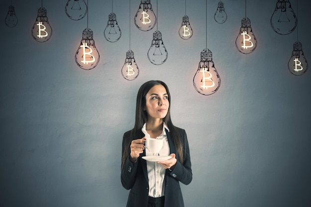 Portrait of a young businesswoman with a cup of coffee and lightbulbs hanging above her head Idea concept