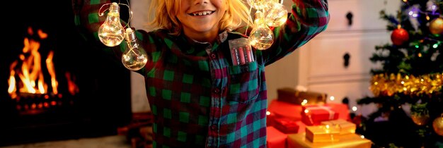 Photo portrait of a young caucasian boy playing with string lights in his sitting room at christmas time