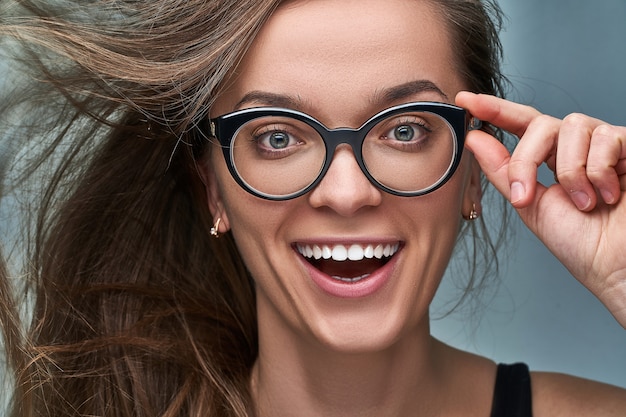 Portrait of young caucasian brunette happy female with surprised joyful amazed excited shocked face expression in black frame glasses with mouth open in surprise. Wow and omg