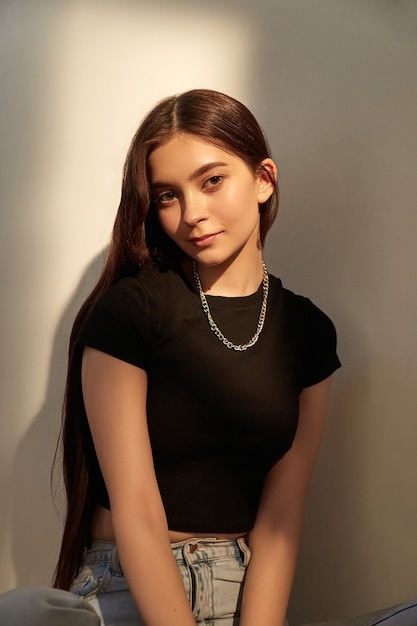 Portrait of young caucasian girl with long hair in jeans sitting next to wall