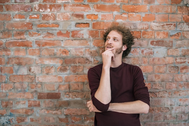 Portrait of young caucasian man with thoughtful expression against the brick wall in the street. Urban concept.