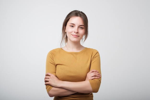 Portrait of young caucasian woman in yellow shirt casually standing near gray wall