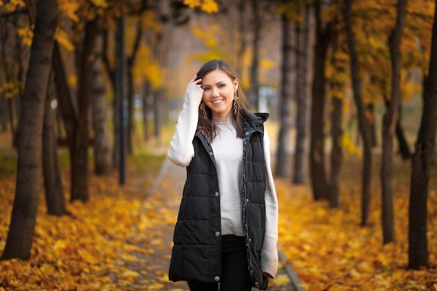 Portrait of a young Central Asian woman in an autumn park on an alley with fallen autumn leaves