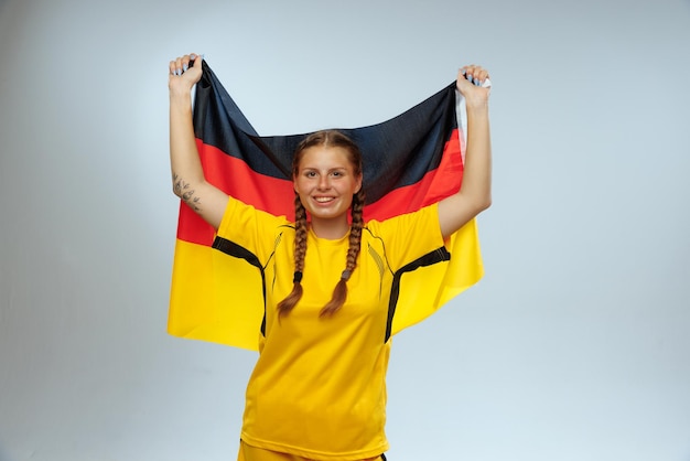 Portrait of young cheerful woman supporting german football team posing isolated over blue background