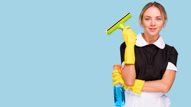 Portrait of young cleaner woman holding plastic wiper and detergent bottle looking at camera