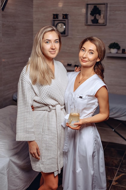 The portrait of a young client and an experienced cosmetologist standing next to her in a spa salon