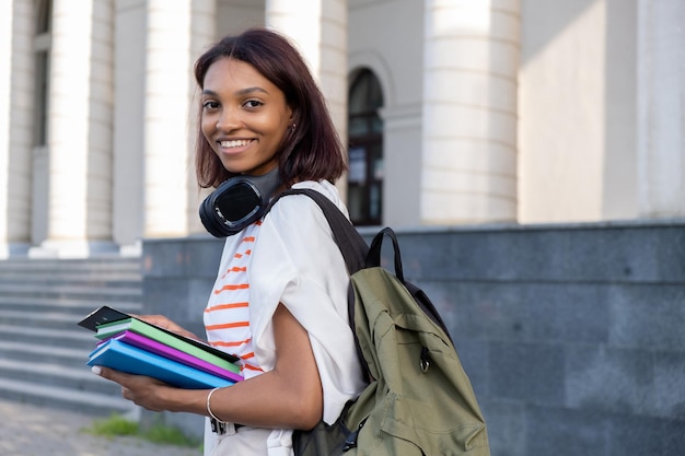 Portrait of a young college girl holding folders and notebooks and walking down the street to go to school or college Student girl smiling and happy