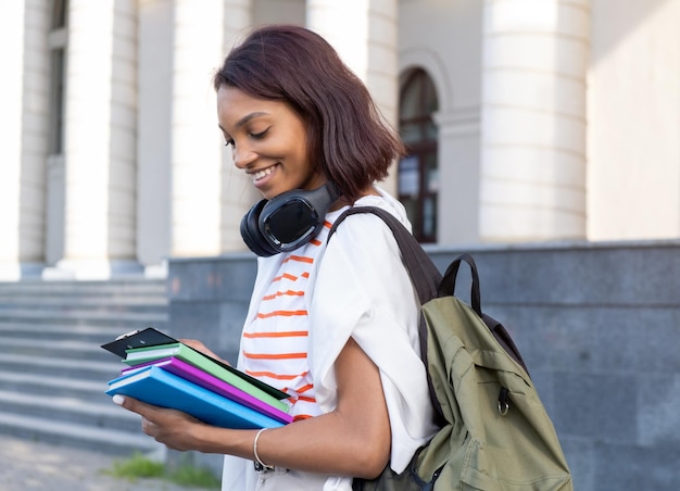 Portrait of a young college girl holding folders and notebooks and walking down the street to go to school or college Student girl smiling and happy