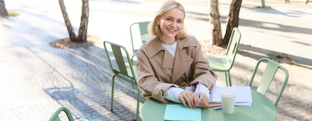 Portrait of young concentrated woman doing homework in a cafe writing in notebook working with