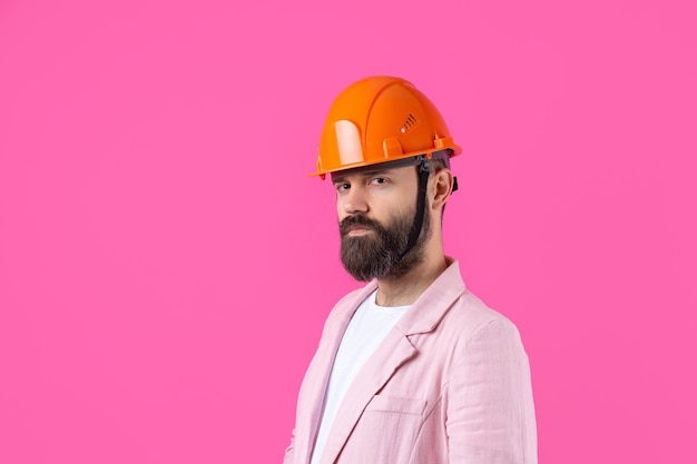 Portrait of young construction engineer wear orange hard hat in a pink jacket standing on red studio background