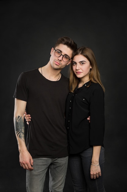 Portrait of young couple in black clothes wearing trendy glasses and posing over black background.