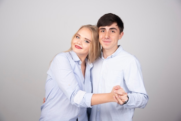 Portrait of a young couple dancing and posing on gray wall.