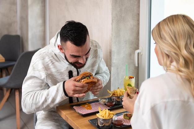 Portrait of Young Couple Eating Hamburger in Restaurant and Drinking Cocktail Passion Fruit Mojito