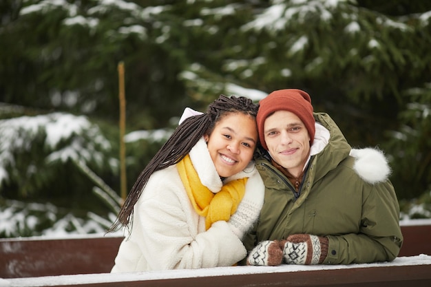 Portrait of young couple embracing and smiling at camera sitting at the table with snowy trees in the background