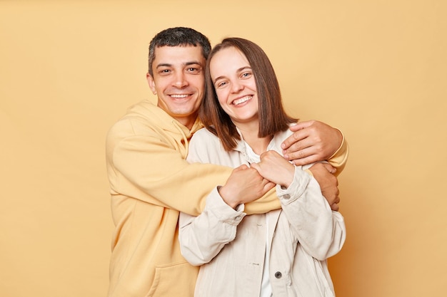 Portrait of young couple smiling isolated over beige background expressing love and gentle being in good mood enjoying spending time together