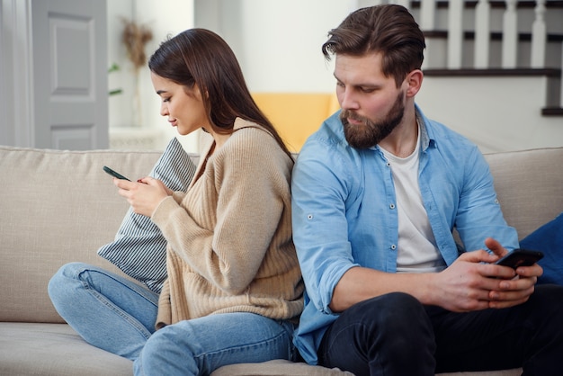 Portrait of young couple standing back to each other and looking at the phone.