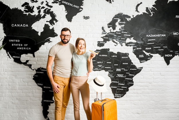 Portrait of a young couple of travelers standing indoors on the world map background ready for a summer vacation