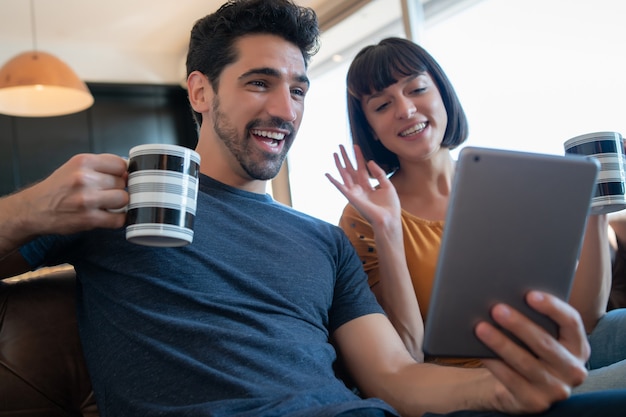 Portrait of young couple on a video call with digital tablet while sitting on couch at home