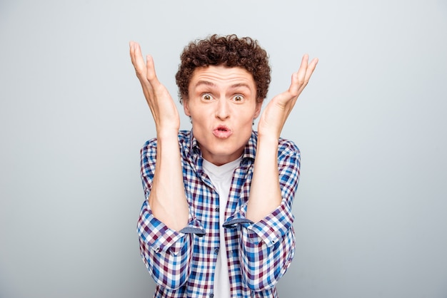 Portrait of young crazy guy raise his hands isolated on gray