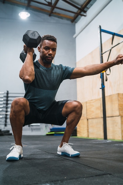 Portrait of young crossfit athlete doing exercise with dumbbell at the gym