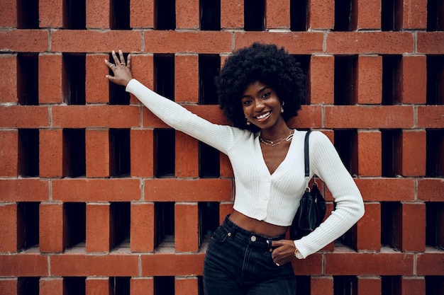 Portrait of young curly charming black female standing against brick wall