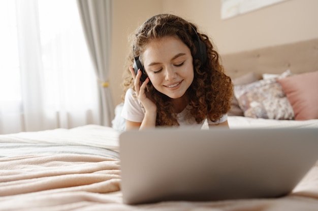 Portrait of a young curly woman using laptop in bed at home