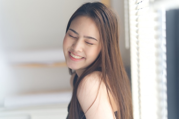 Portrait of young cute Asian girl closing her eyes with smile standing next to the window 