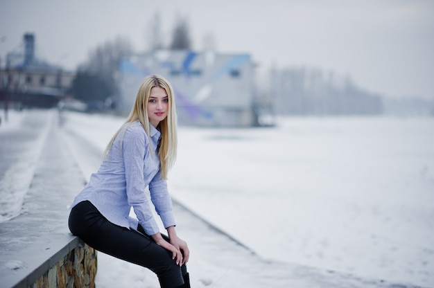 Portrait of young cute blonde woman on blouse at pier, foggy river on winter ice. 