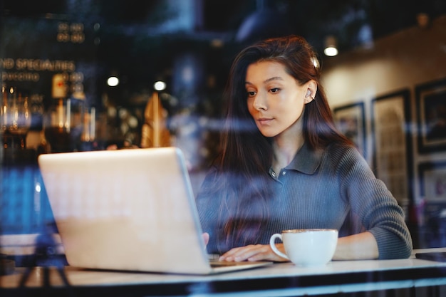 Portrait of young cute girl drinking coffee and using laptop at a cafe