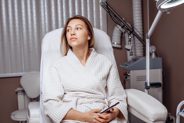 Portrait of a young cute girl in a white coat sitting in a cosmetology chair in the office of a beauty salon