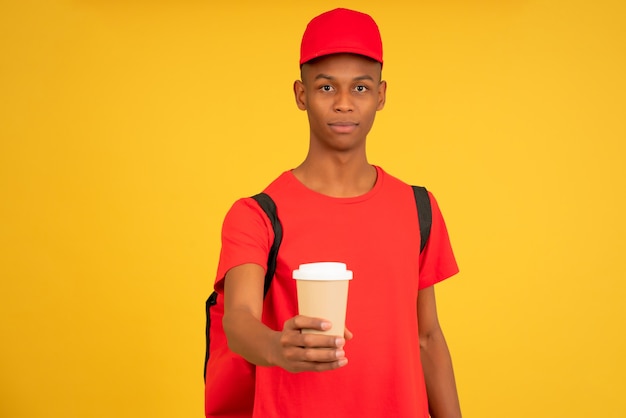 Portrait of young delivery man holding a cup of a takeaway coffee. Delivery service concept.