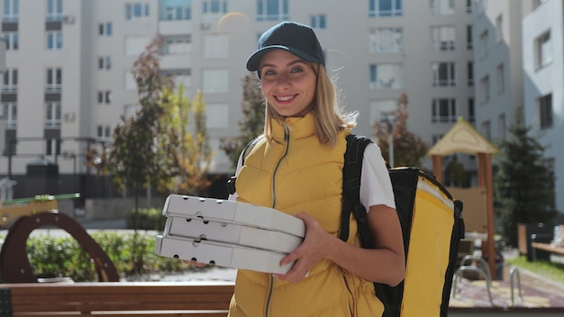 Portrait of young delivery woman in yellow uniform with pizza boxes looking at camera and smile and waiting for customer Delivery service takeaway orders