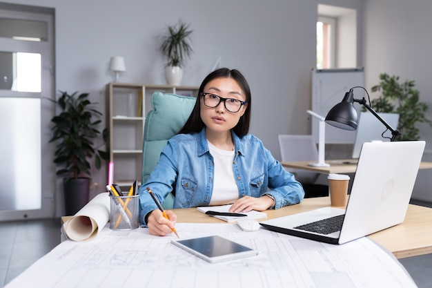 Portrait of young designer woman in modern office at work successful asian woman in glasses looking