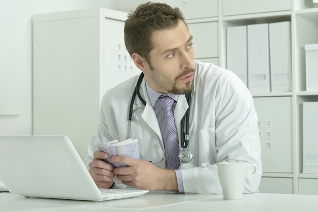 Portrait of young doctor with laptop and money