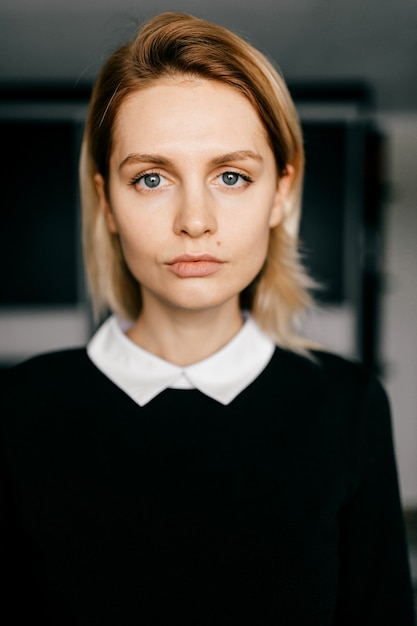 Portrait of young elegant short-haired blond girl in formal black clothes posing indoors