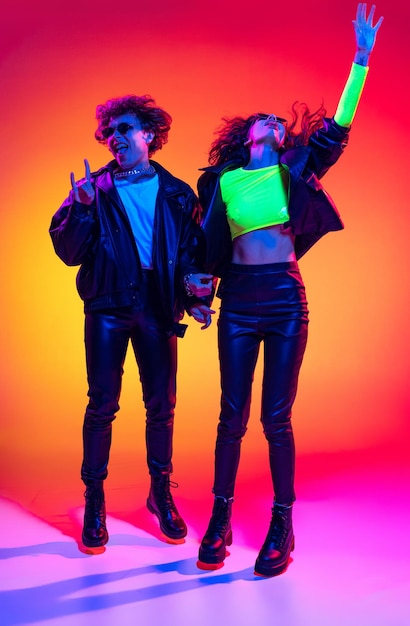 Portrait of young emotive people man and woman jumping isolated over gradient background in neon Rock music