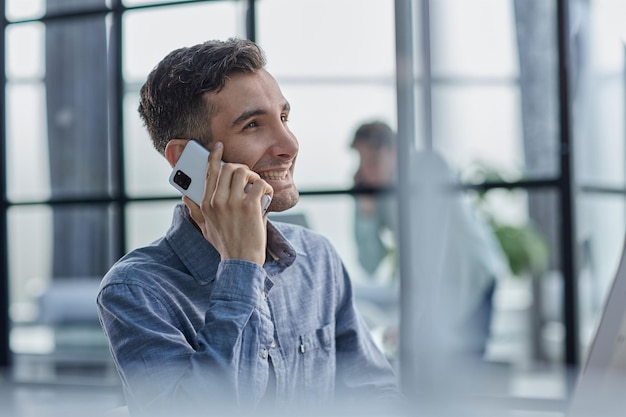 Portrait of young entrepreneur in casual office making phone call while working with laptop