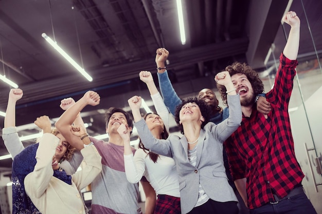 portrait of young excited multiethnics business team of software developers standing and looking at camera while celebrating success at modern startup office