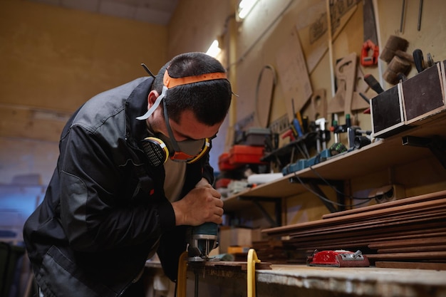 Portrait of young factory worker wearing respirator while sanding wood in workshop copy space