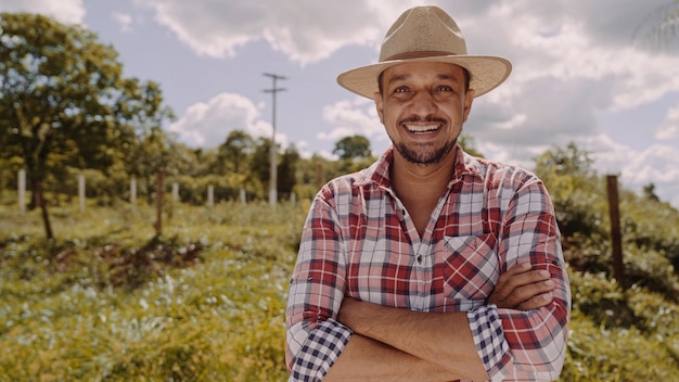 Portrait of young farmer man with crossing hands in the casual shirt and hat in the farm