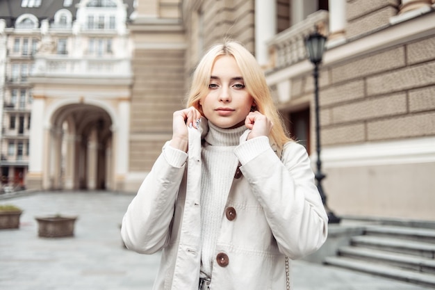 Portrait of a young fashion blonde woman in an autumn trench coat against the background of urban architecture