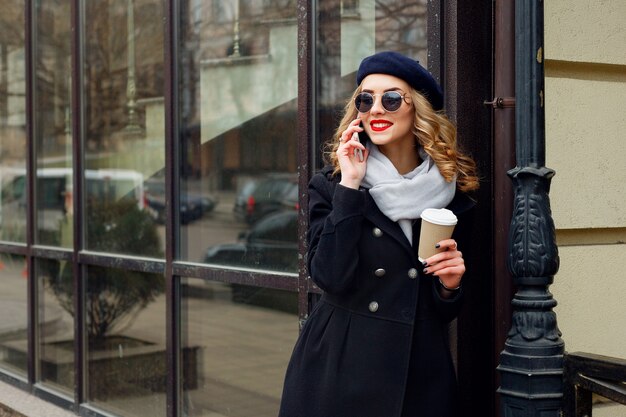 Portrait of young fashionable girl posing on street with paper coffee cup