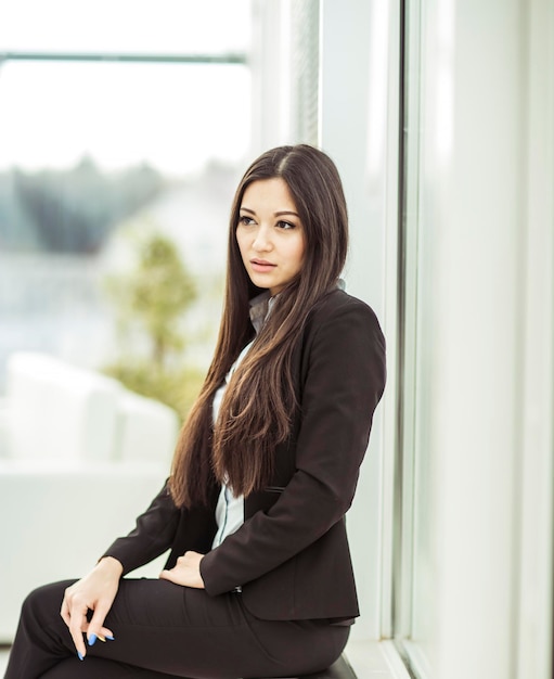 Portrait of a young female assistant next to the window in the office